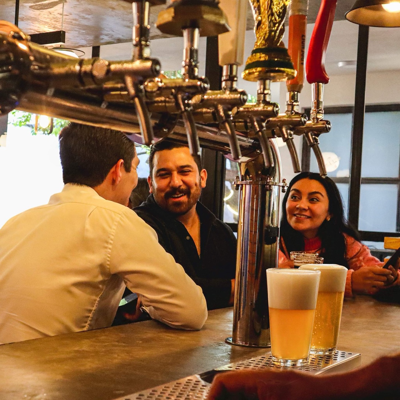 Amigos platican en la barra junto a los grifos de cerveza