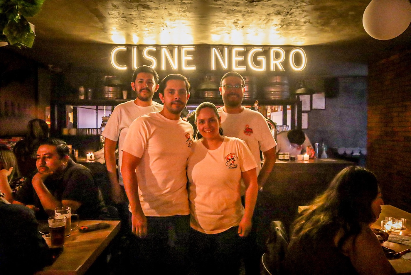 Anfitriones de la Noche de Velas y Pizza posan bajo el letrero de neón