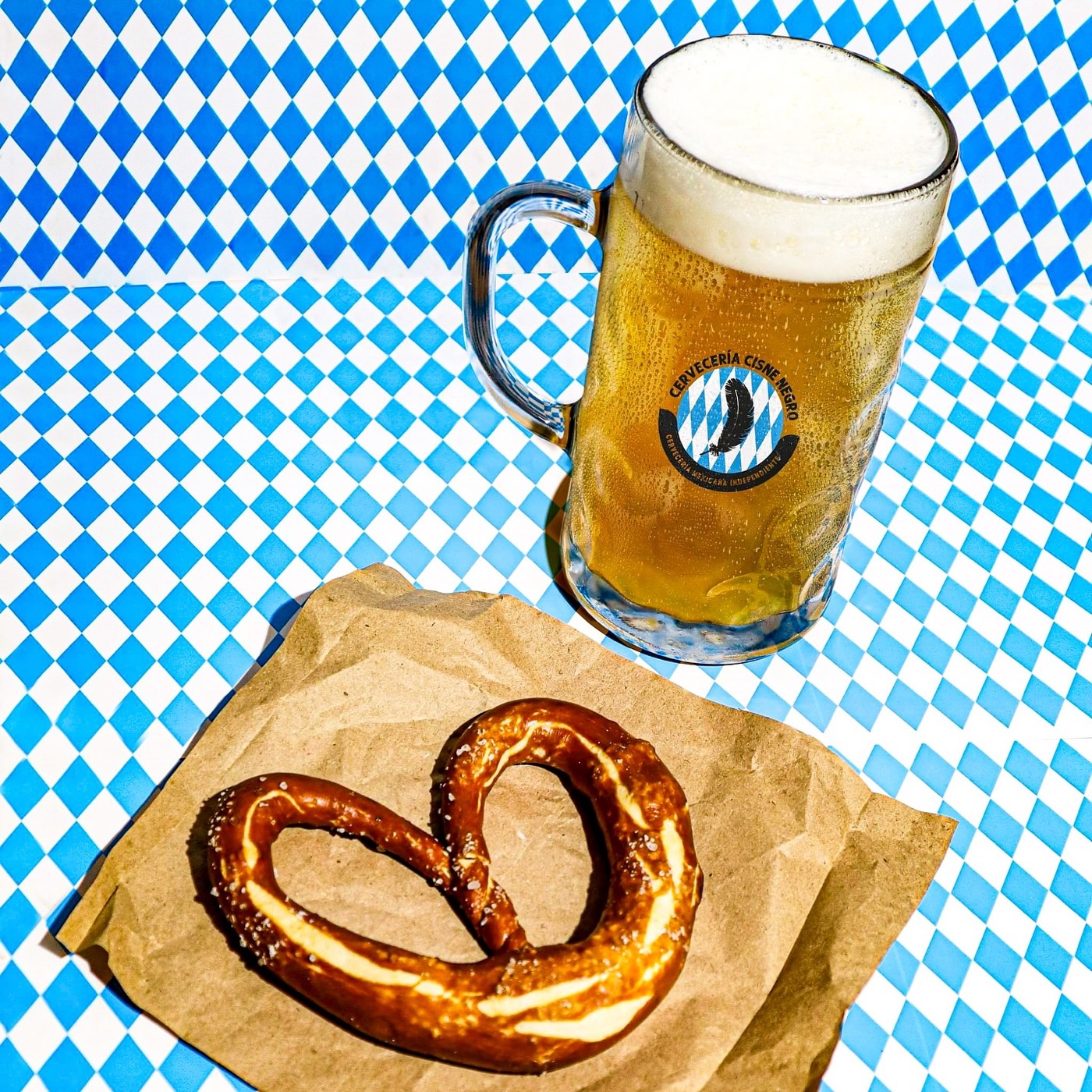 Tarro de cerveza y un pretzel sobre un mantel azul y blanco de Oktoberfest