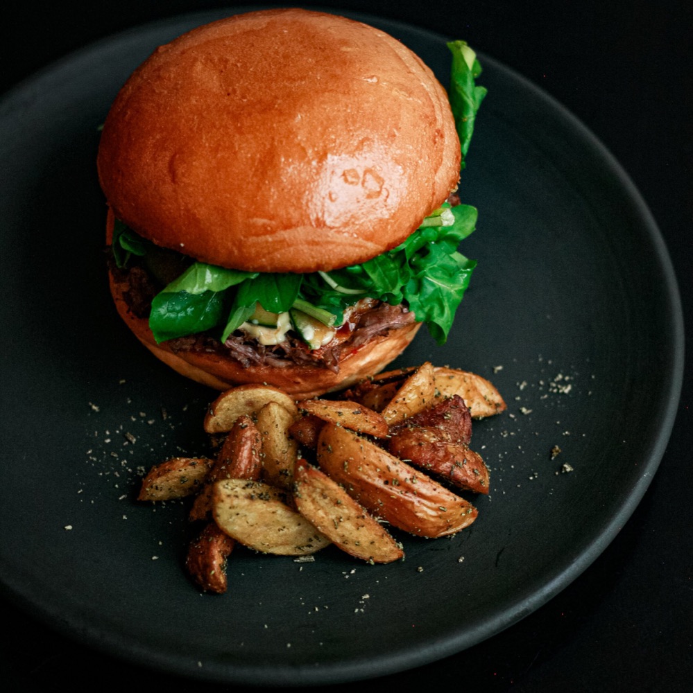 Hamburguesa de costilla de res con arúgula y pepinos encurtidos